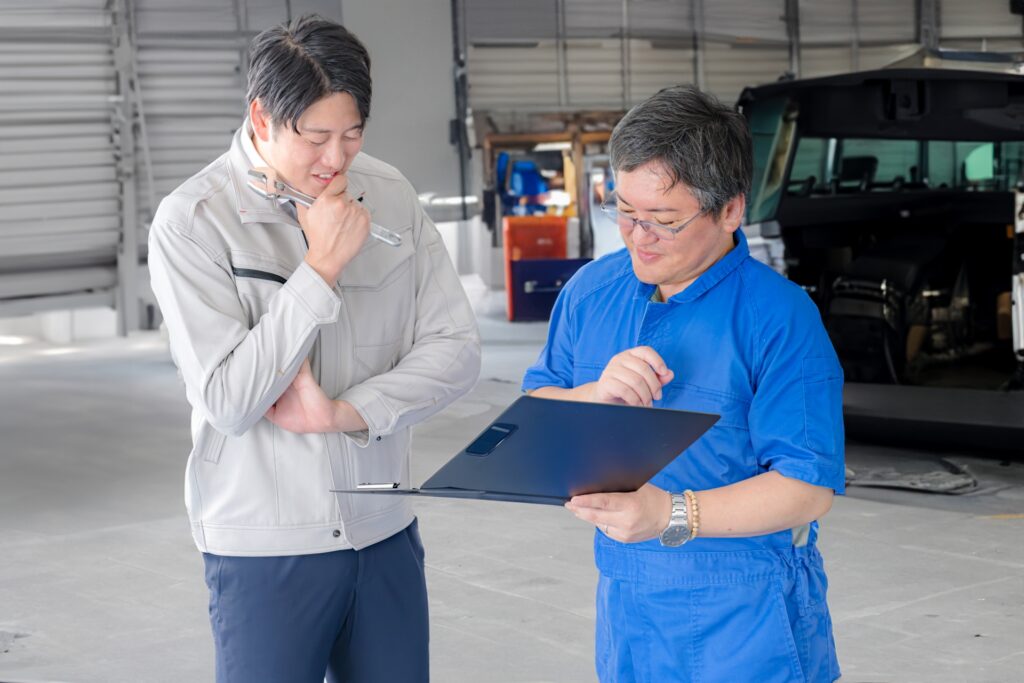 整備工場でクリップボードを見ながら打ち合わせる作業員